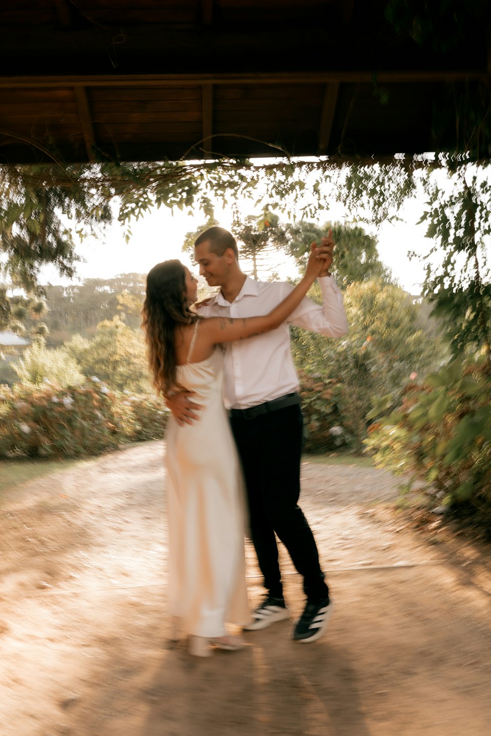 Un couple danse ensemble sur un chemin de terre sous une pergola.