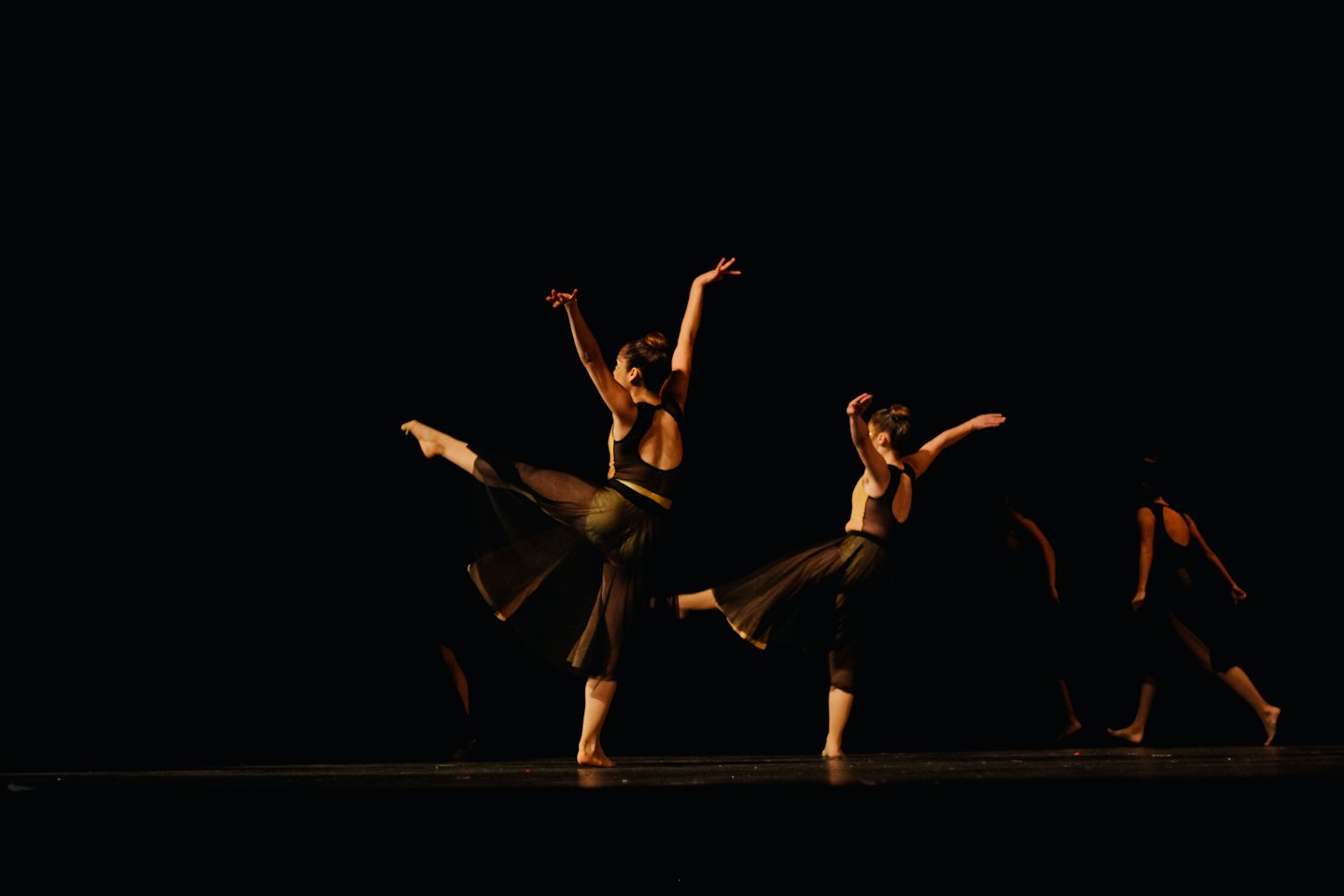 Trois danseurs sur une scène sombre sous les projecteurs.